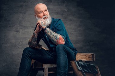 Karanlık arka planda dövmeleri olan şık, yaşlı bir hippi.