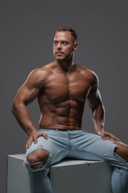 Çıplak vücut geliştirici gri arka planda kutunun üzerinde oturuyor