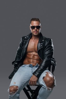 Şık giyinmiş kaslı adam sandalyede oturuyor.