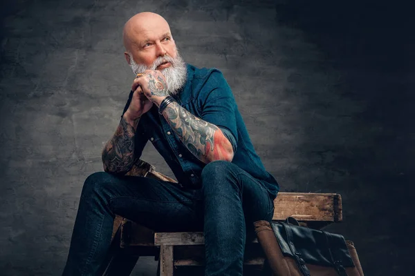 Karanlık arka planda dövmeleri olan şık, yaşlı bir hippi.