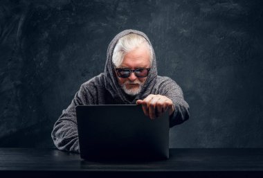 Karanlık arka planda dizüstü bilgisayarı olan yaşlı hacker.