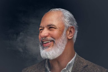 Esmer arka planda bej takım elbiseli, gülümseyen yaşlı adam.