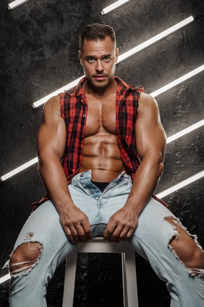 Yırtık pırtık kıyafetler giymiş kaslı yakışıklı bir adam.