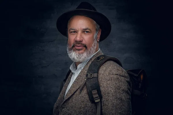 Senior mit Hut und Rucksack vor dunklem Hintergrund — Stockfoto