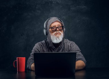 Contemporary elderly hacker with cup and laptop sitting at table