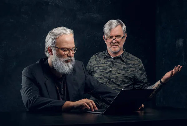 Командна робота двох літніх чоловіків з ноутбуком на темному тлі — стокове фото