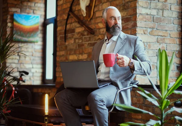 Ofiste laptoplu ve kahve fincanlı yaşlı bir adam var.
