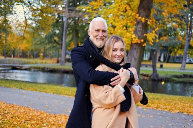 Gündüz vakti dışarıda yaşlı bir adamla genç bir kadına sarılıyor.