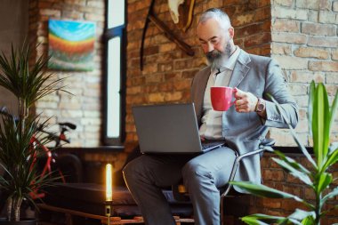 Ofiste laptoplu ve kahve fincanlı yaşlı bir adam var.