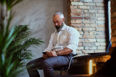 Ofisteki koltukta oturan üst düzey bir adam cep telefonu kullanıyor.