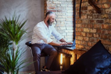 Ofisin penceresinde dizüstü bilgisayarı olan yaşlı bir işadamı.