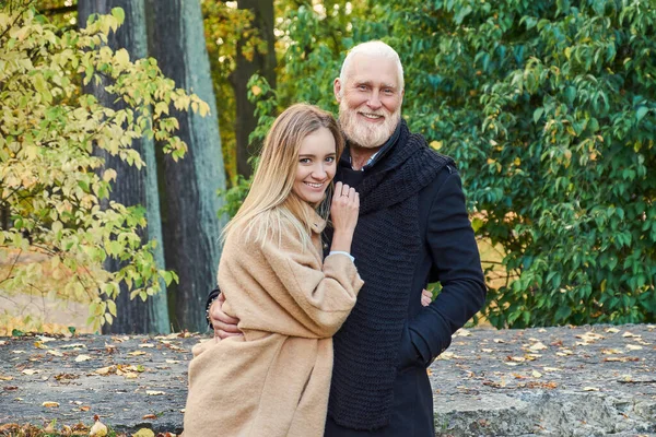 Cheerful senior man cuddling his young girlfriend in autumn — стоковое фото