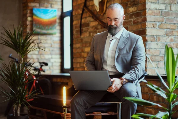 Ofisteki koltukta dizüstü bilgisayar kullanan zarif yaşlı bir adam.
