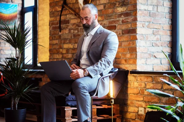 Eleganter älterer Mann sitzt mit Laptop auf Stuhl im Büro — Stockfoto
