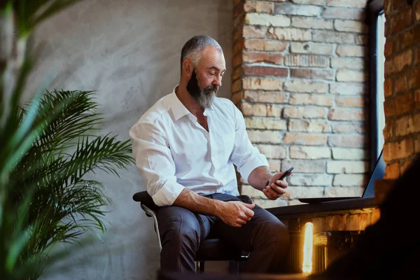 Ofisteki koltukta oturan üst düzey bir adam cep telefonu kullanıyor.