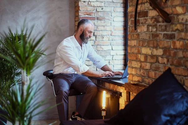 Ofisin penceresinde dizüstü bilgisayarı olan yaşlı bir işadamı.