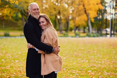 Cuddling old man and young woman outdoors in fall in daytime
