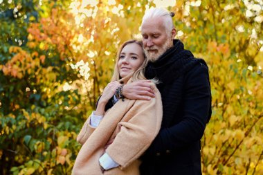 Gündüz vakti dışarıda yaşlı bir adama ve genç bir kadına sarılıyor.