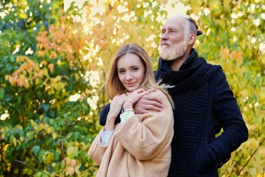 Gündüz vakti dışarıda yaşlı bir adama ve genç bir kadına sarılıyor.