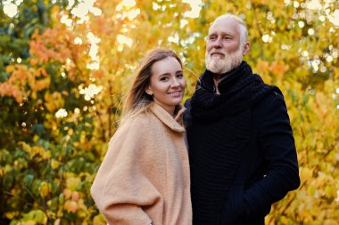 Sonbaharda genç kız arkadaşına sarılan yaşlı adam.