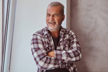 Happy senior man dressed in plaid shirt near window