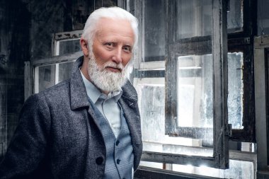 Elegant senior man dressed in coat against lot of windows
