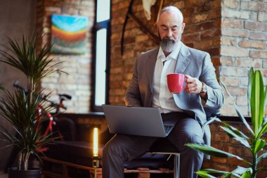 Ofiste laptoplu ve kahve fincanlı yaşlı bir adam var.