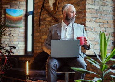 Ofiste laptoplu ve kahve fincanlı yaşlı bir adam var.