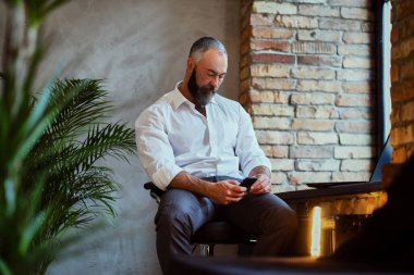 Ofisteki koltukta oturan üst düzey bir adam cep telefonu kullanıyor.