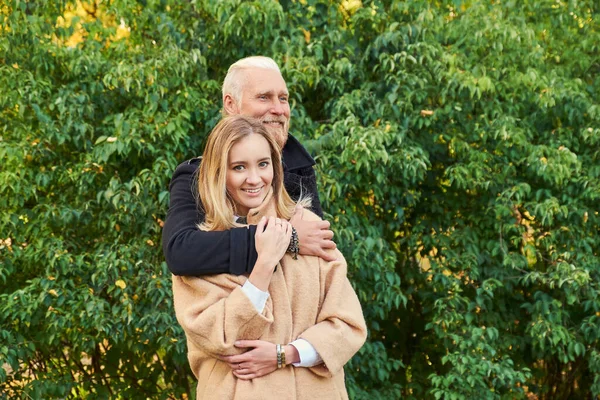 Веселый пожилой мужчина обнимает свою внучку осенью — стоковое фото