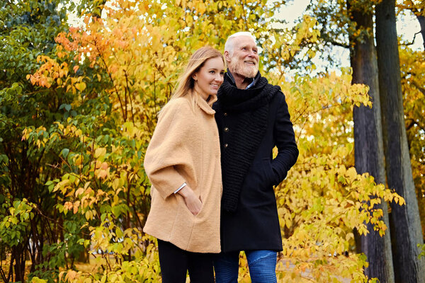 Cheerful granddaughter and grandfather on walk in autumnal wood