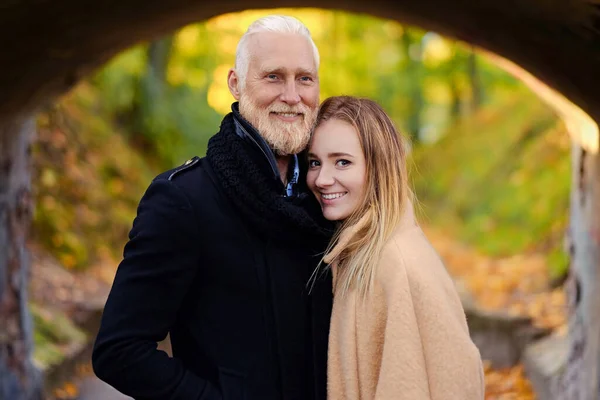 Alegre hombre mayor abrazando a su novia bajo el arco en otoño —  Fotos de Stock