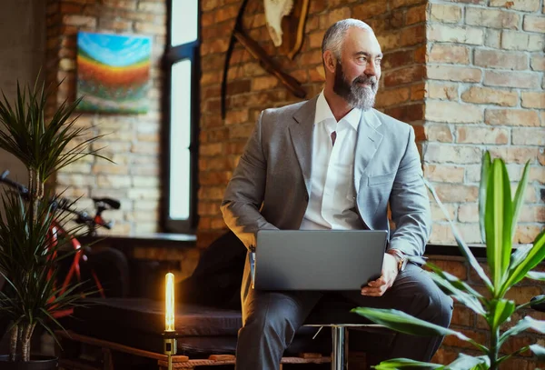 Elegant elderly man using laptop sitting on chair in office — Stockfoto