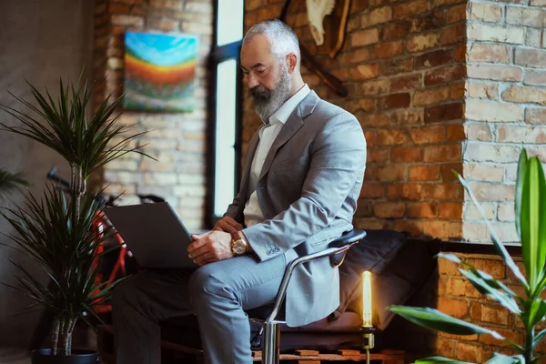 Elegant äldre man med bärbar dator sittande på stol på kontoret — Stockfoto