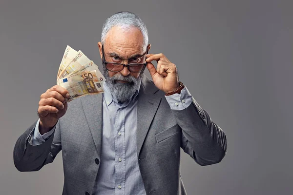 Old man with money staring at camera against grey background — 스톡 사진