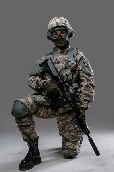 Сучасна сержантка з рушницею сидить на сірому фоні — стокове фото