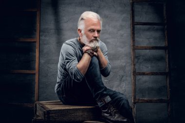 Yakacak odununda oturan, gri gömlekli, tahta merdivenli, modaya uygun yaşlı bir adamın fotoğrafı..