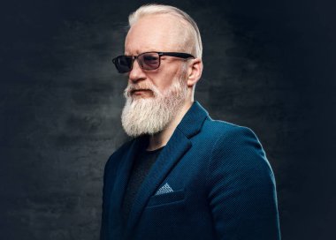 Pahalı bir takım elbise ve güneş gözlüğü takmış, koyu renk arka planda poz veren şık bir son sınıf öğrencisi..