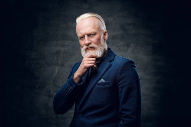 Stüdyoda, koyu arkaplan karşısında mavi takım elbiseli, şık saç stili olan düşünceli son sınıf öğrencisinin fotoğrafı..