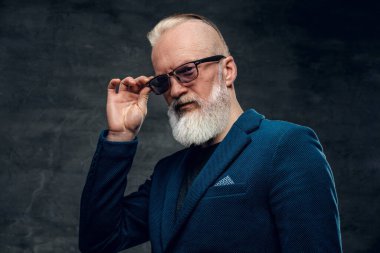 Pahalı bir takım elbise ve güneş gözlüğü takmış, koyu renk arka planda poz veren şık bir son sınıf öğrencisi..