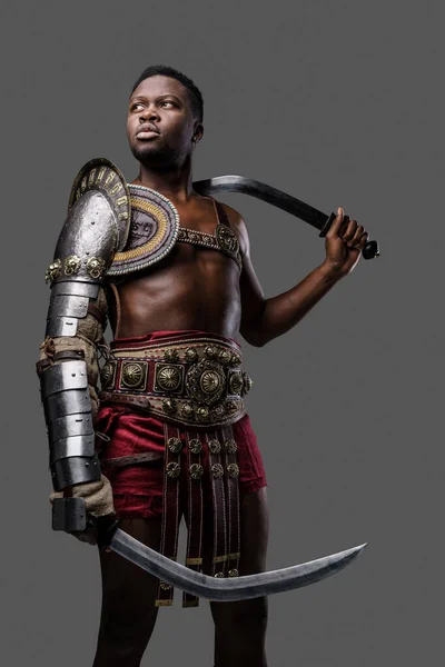 灰色の背景に隔離された双子の剣を持つアフリカの民族の古代剣闘士のショット — ストック写真