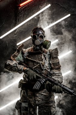 Gaz maskeli ve tüfekli bir Afrikalı askeri vurularak esmer arka plana karşı neon ve dumanlı.
