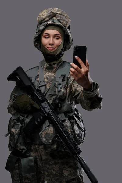 Portrait of joyful woman soldier dressed in camouflage clothes making selfie.