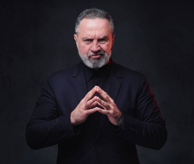 Siyah giyinmiş, siyah arka planda poz veren dalgın kıdemli bir adamın fotoğrafı..