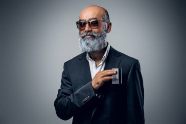 Şık takım elbiseli ve banka kartlı güneş gözlüklü kıdemli işadamının fotoğrafı..