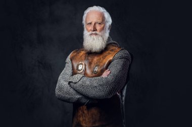 Kendine güveni tam, antika zırh giymiş, karanlık arka planda çapraz kolları olan yaşlı bir savaşçı..