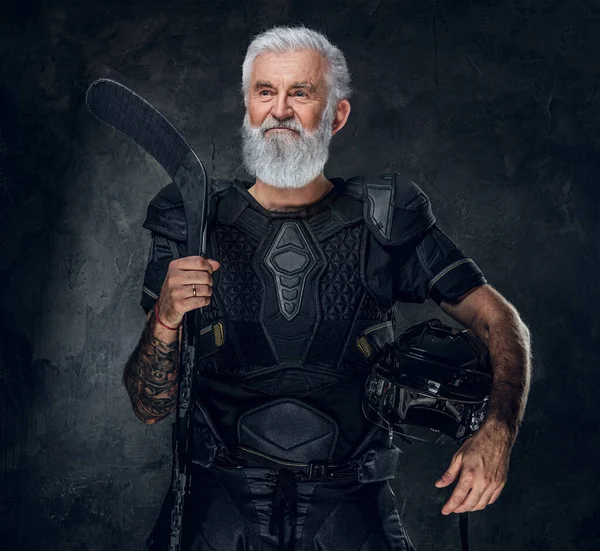 Shot of active old man dressed in black uniform holding helmet and hockey stick.