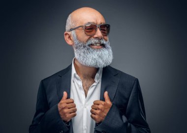 Paltolu ve beyaz gömlekli neşeli yaşlı adam portresi gri arka plana bakıyor..