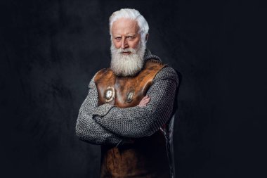 Kendine güveni tam, antika zırh giymiş, karanlık arka planda çapraz kolları olan yaşlı bir savaşçı..