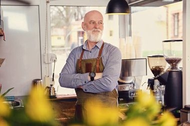 Önlük ve gömlek giymiş kollarını kavuşturmuş sakallı yaşlı barmenin portresi..